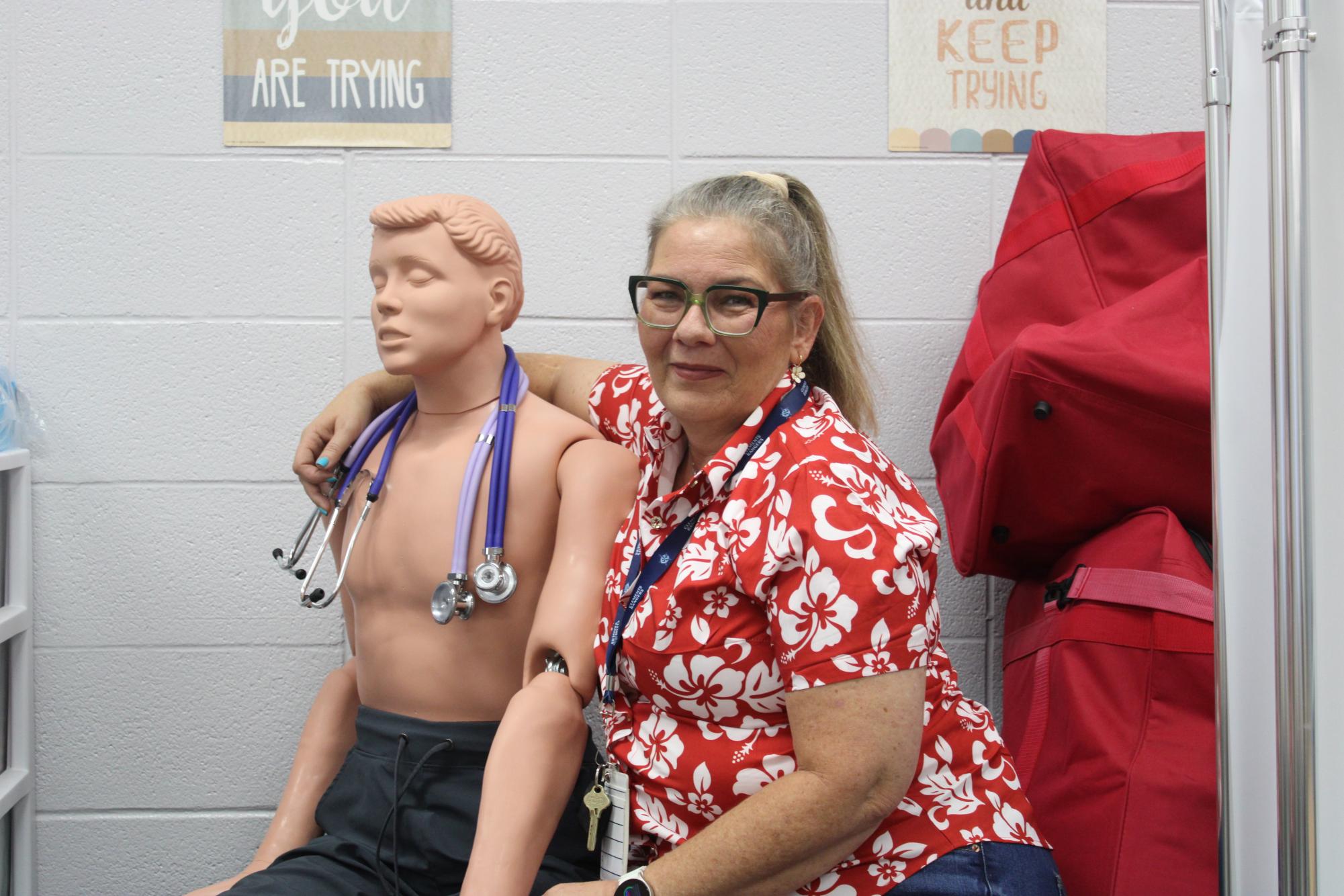 Health science teacher Staci Mikeska with an arm slung around a manikin. 