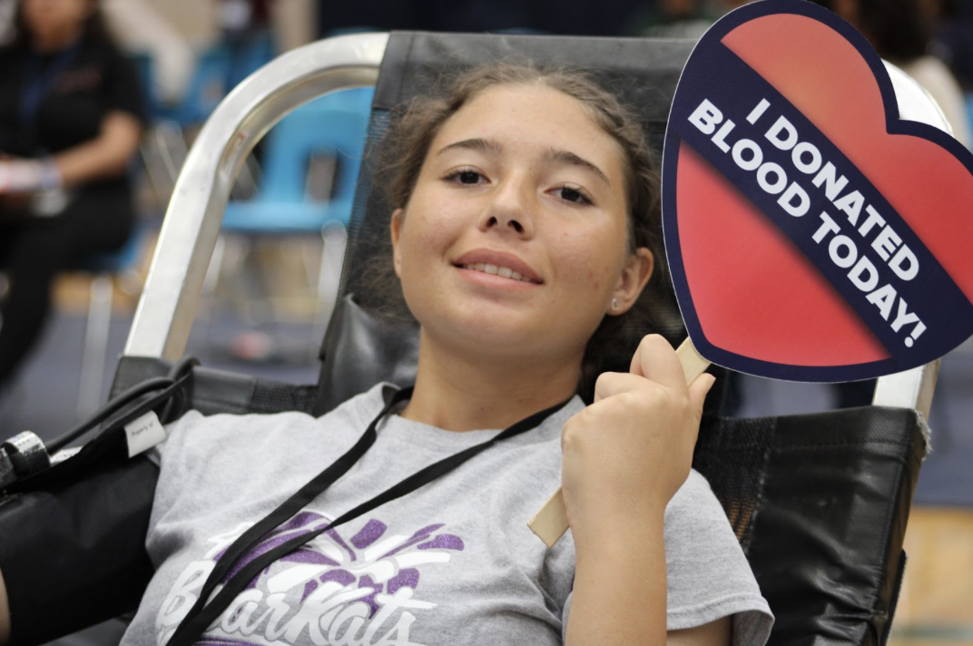 A student holding up a donation sign after getting her blood drawn.