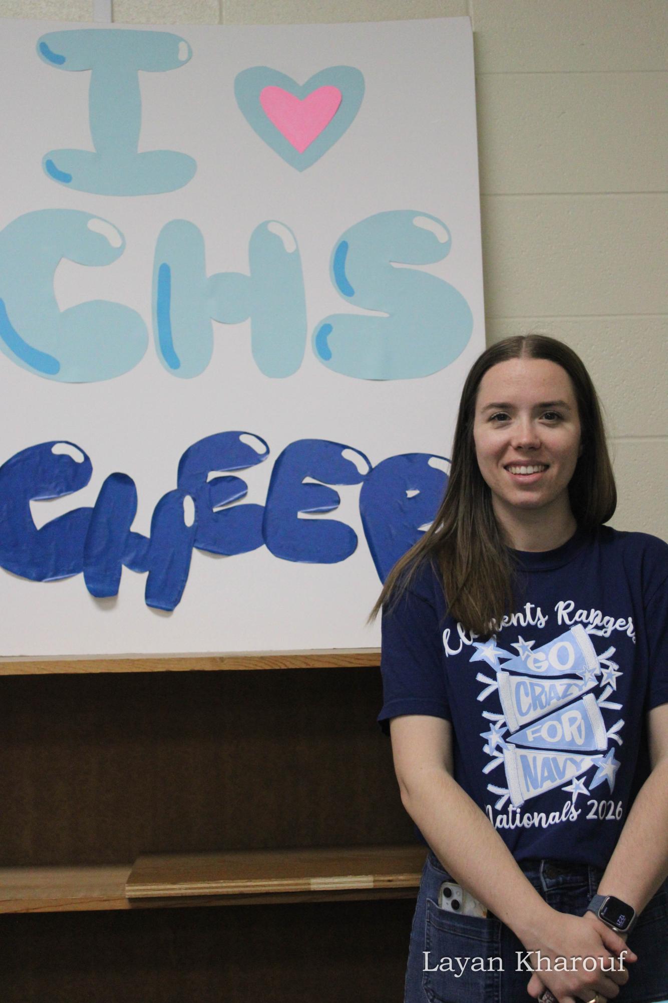 Cheer coach and Chemistry teacher Katherine White in front of an, “I [heart] CHS Cheer” poster.